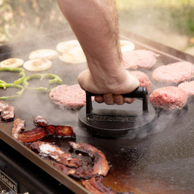 Cuisinart cast iron press in an outdoor cooking setup for versatile grilling.