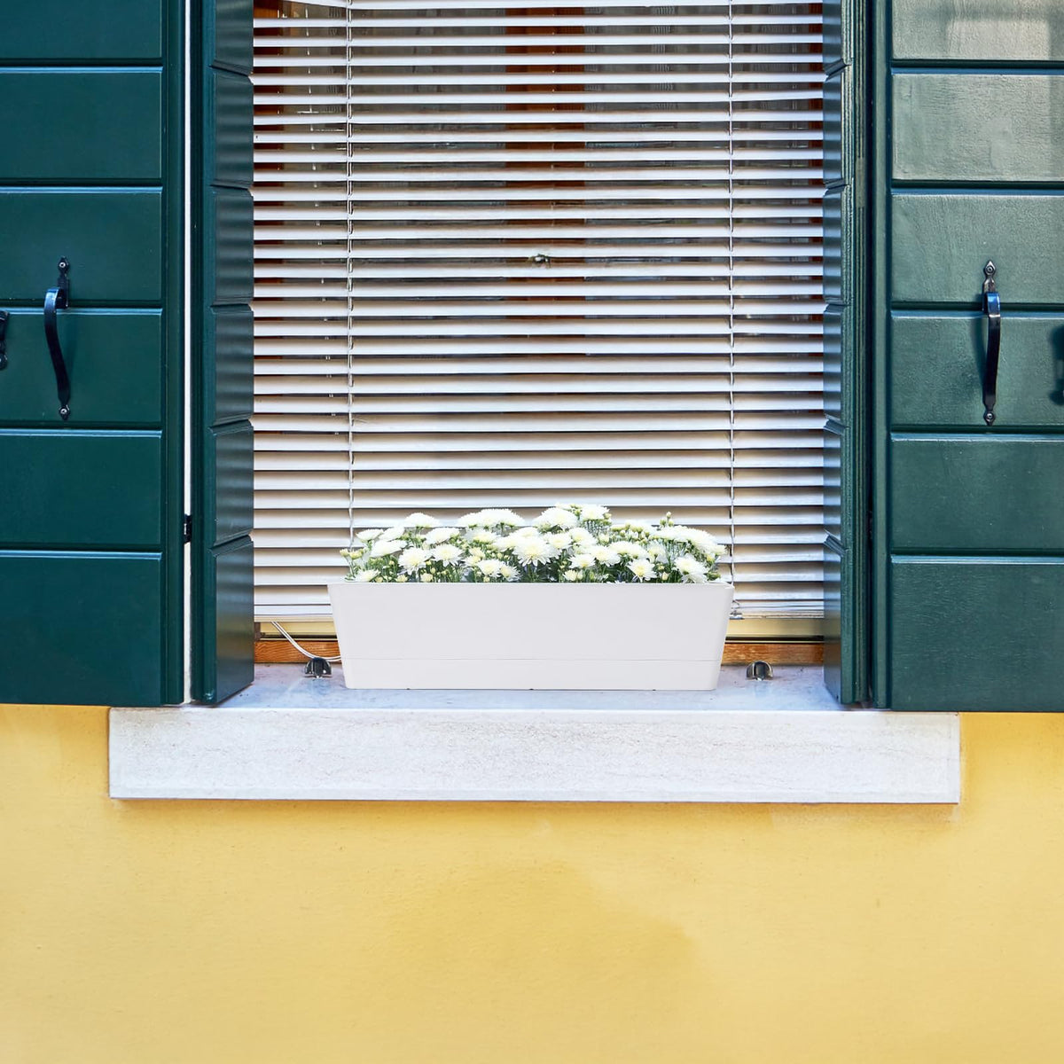 Outdoor balcony scene featuring GREANER planter with drainage holes.