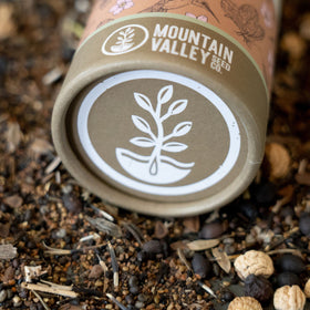 Seeds from Mountain Valley Wildflower Seed Shaker spread on soil ready to germinate.