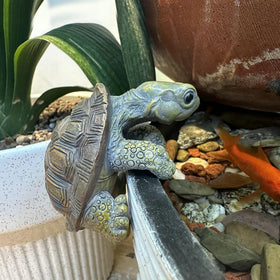 TSCVPJL Turtle figurine climbing the edge of a vase or fence.