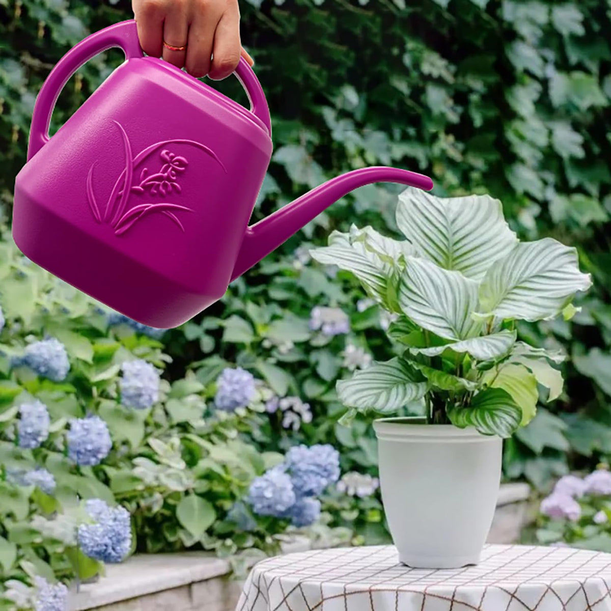 VKPLITE Rose Red watering can in use beside potted plants on a balcony.